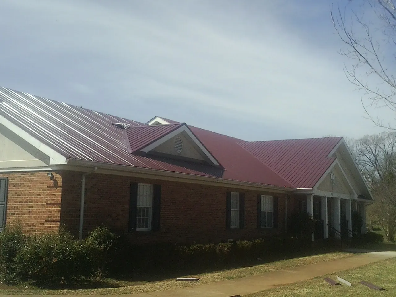 Red metal roof with gabled entries on a long brick building, from a Hail Damage Roof Repair job in Stendal