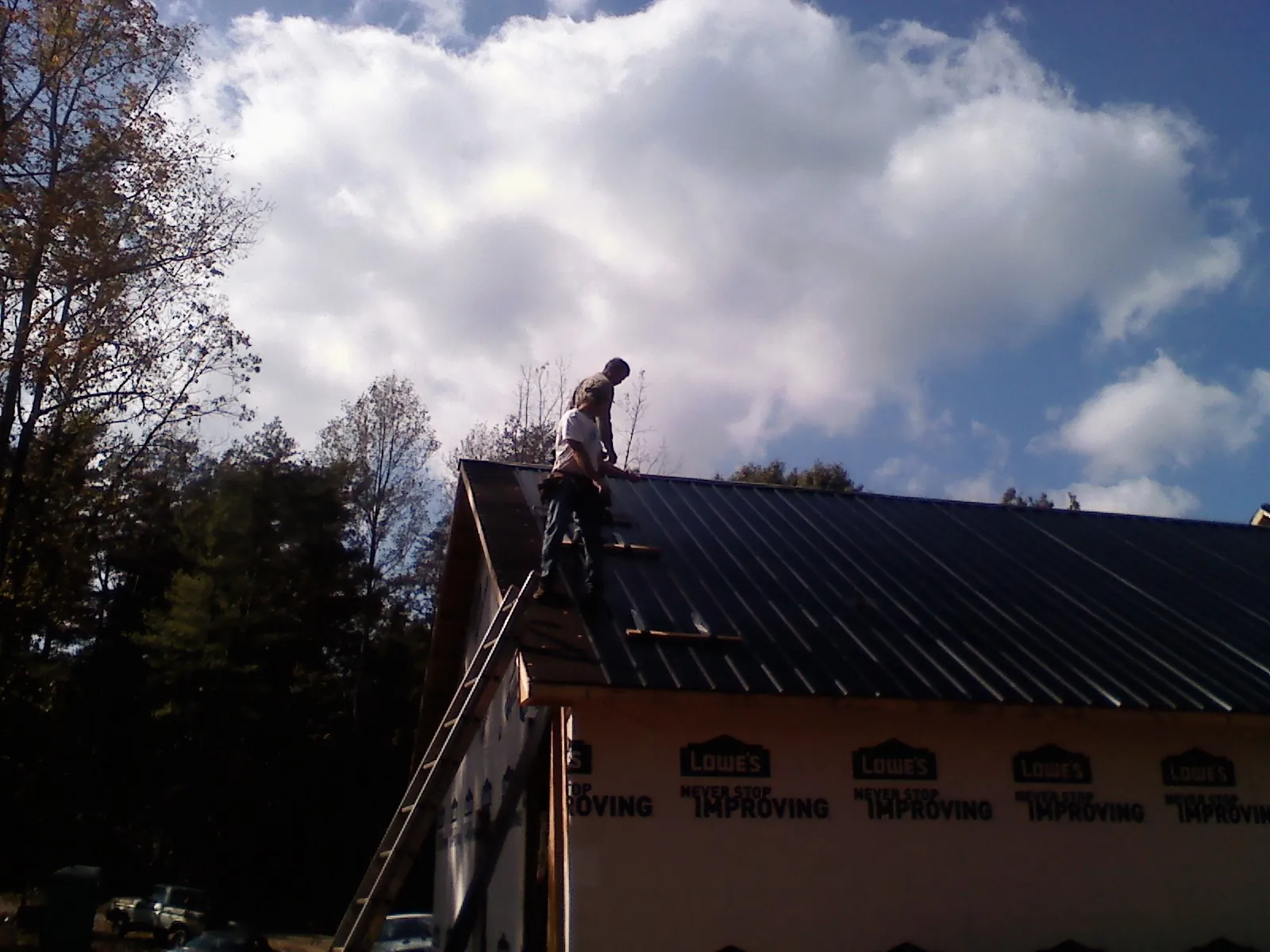 Roofer fastening dark metal panels high against a cloudy sky, from a Roof Inspection job in Stendal