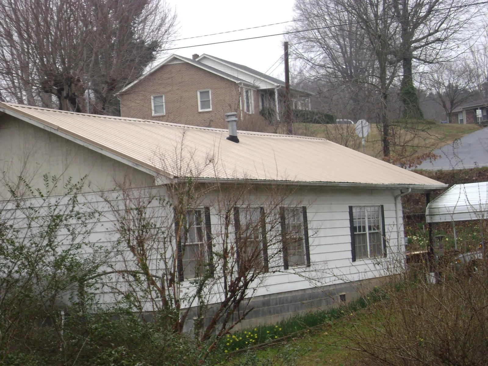 Tan metal roof on a white sided house set into a hillside — Commercial Roofing by Roofing Brothers in Stendal